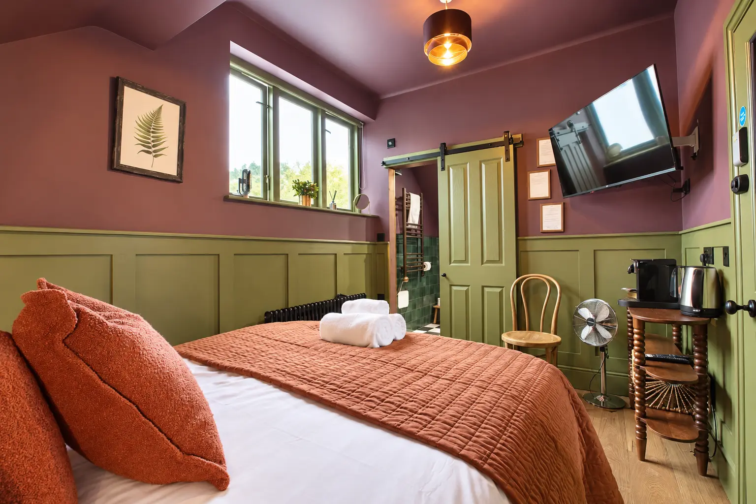 Room 3 at The Linen Rooms — king bed seen toward the window, with the olive barn door open to the green-tiled ensuite